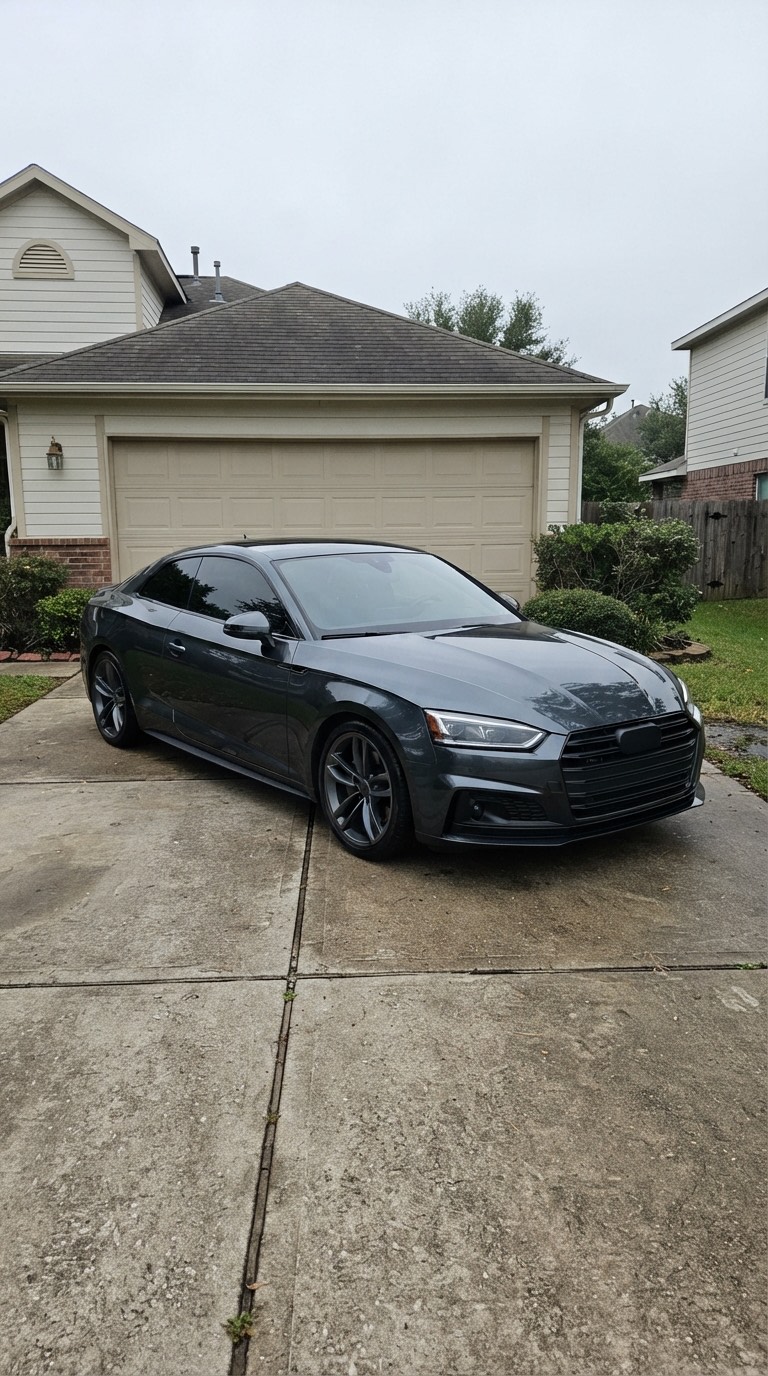 Phone shot of a grey coupe parked in a suburban driveway